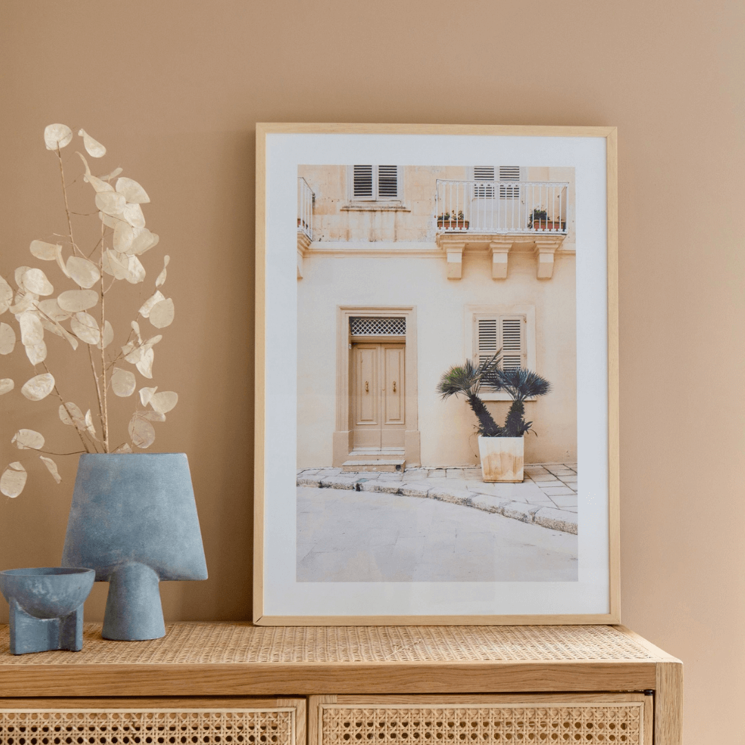 Fotovergroting Posterframe Portrait 3:4 in houten frame met foto van een beige gevel in een warm interieur.