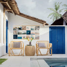 Instawall Tuinposter Wide 2:1 fotocollage als tuinwanddecoratie aan witte muur met wickerstoelen en blauwe deuren