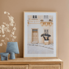 Fotovergroting Posterframe Portrait 3:4 in houten frame met foto van een beige gevel in een warm interieur.